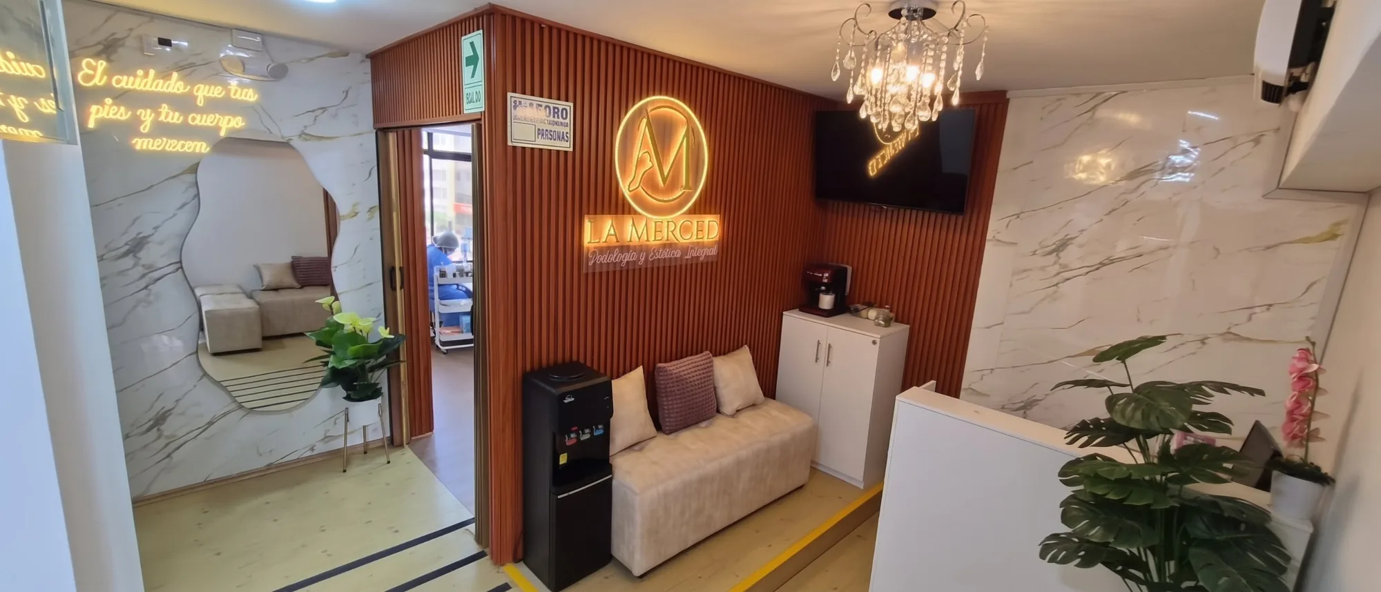 Recepción de Podología La Merced: sala de espera con el logo iluminado, paredes de mármol y un sofá